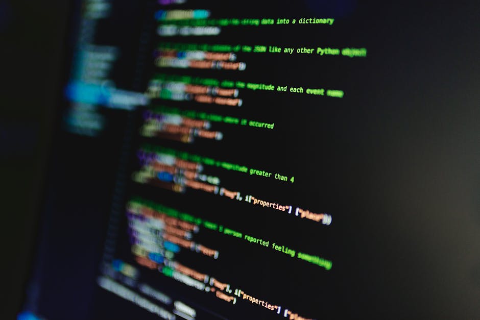 A close-up photograph of a computer screen displaying lines of colorful programming code, with text in shades of green, pink, blue, and white against a dark background. The code appears to be part of